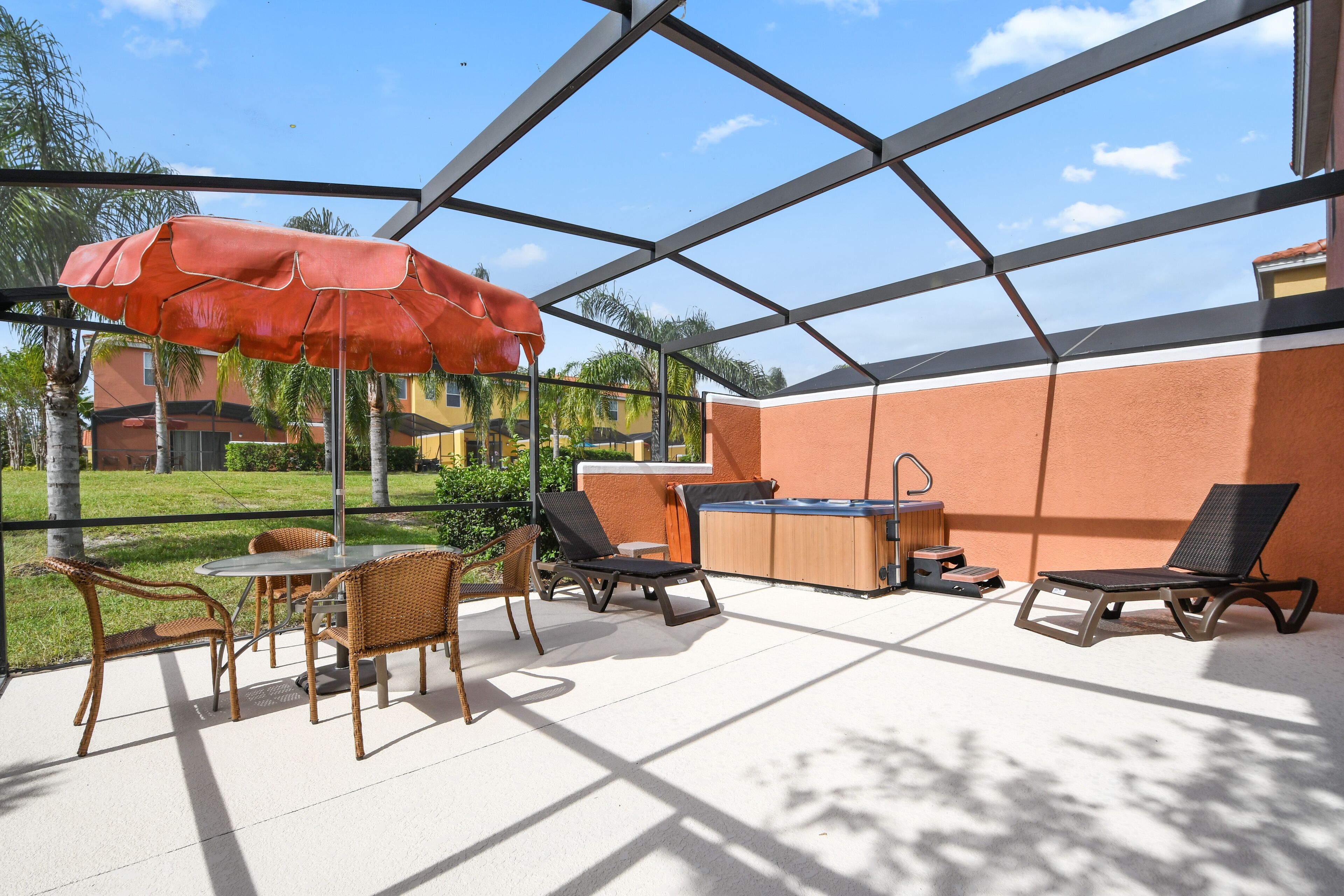 Une terrasse extérieure avec une table et des chaises, un parasol rouge et un jacuzzi.