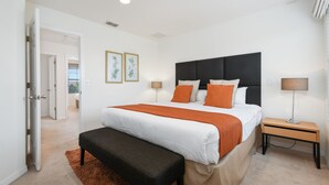 Un dormitorio con una cama grande, una mesita de noche, un banco y una puerta que da a otra habitación.