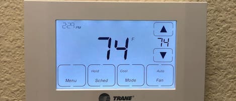 A TRANE HVAC control panel with a digital display showing 74°F, a pink maintenance tag, and operational buttons.