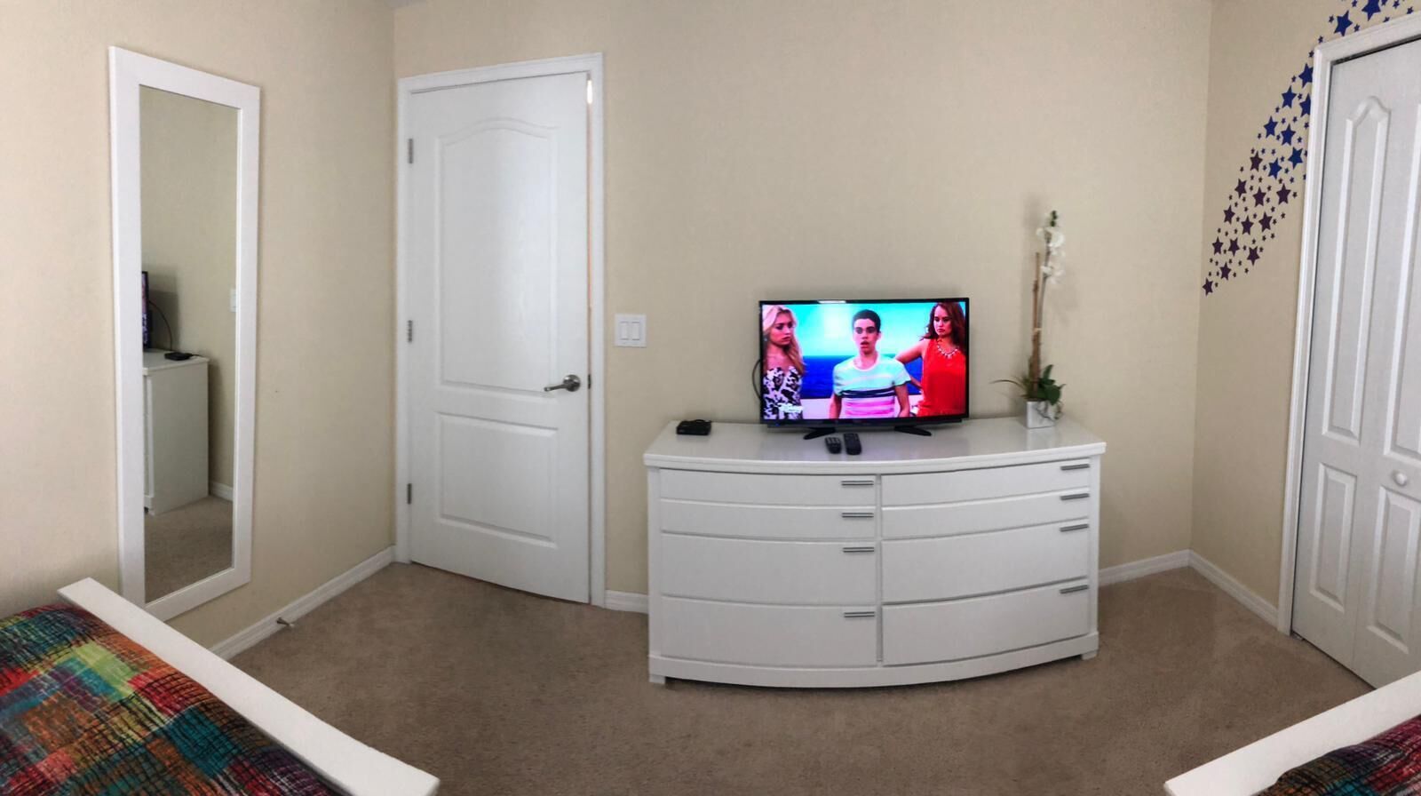 A bedroom with a bed, a white dresser, a television, and a door.