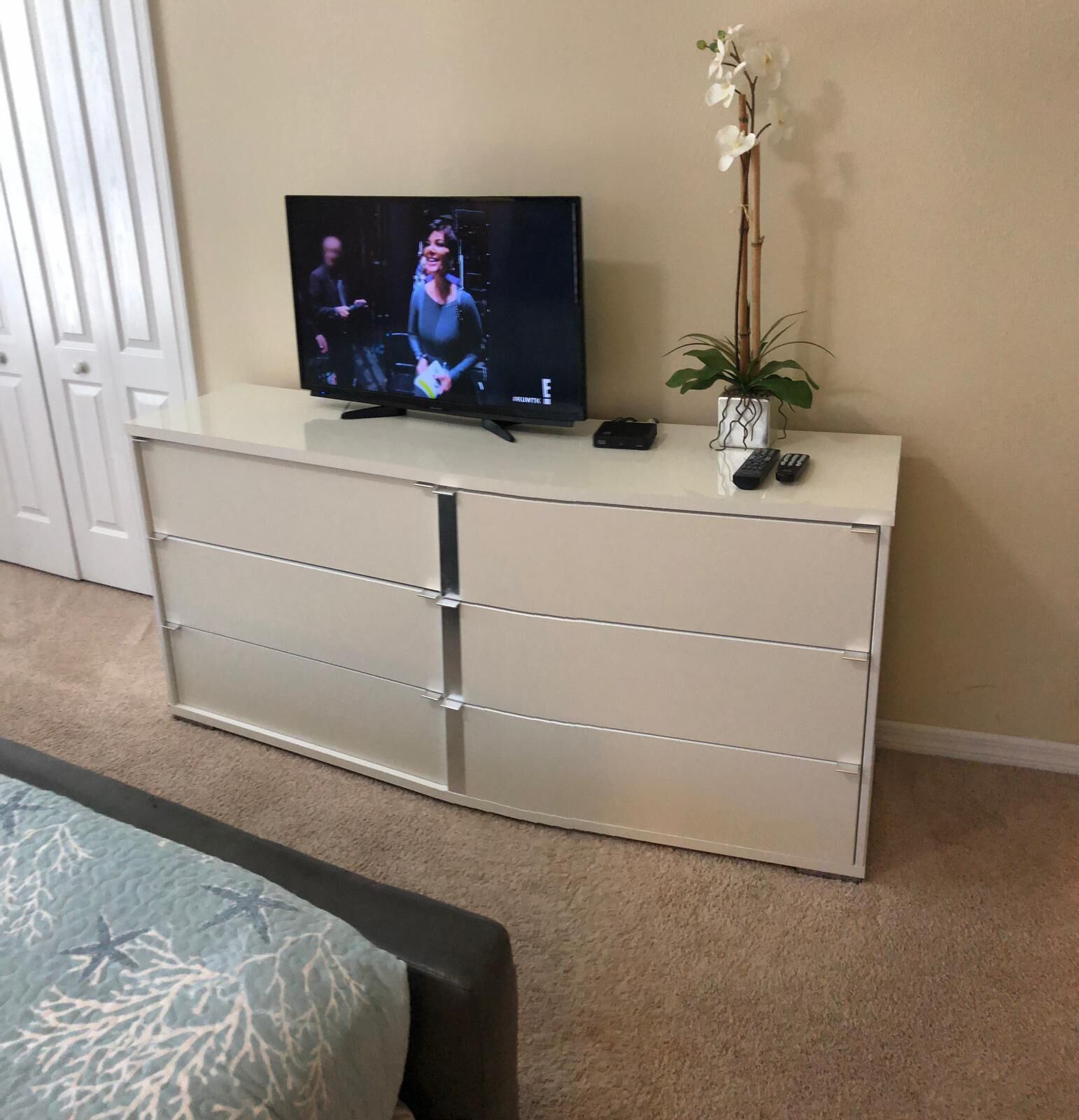 A television on a white cabinet with a remote control and a plant beside it.