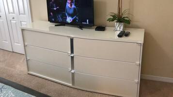 A television on a white cabinet with a remote control and a plant beside it.