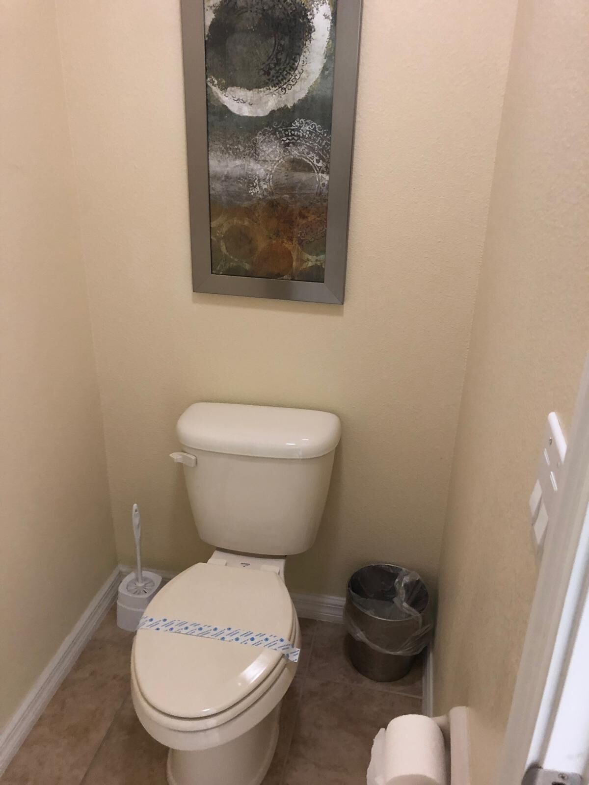 A small bathroom with a toilet, a trash can, and a painting on the wall.