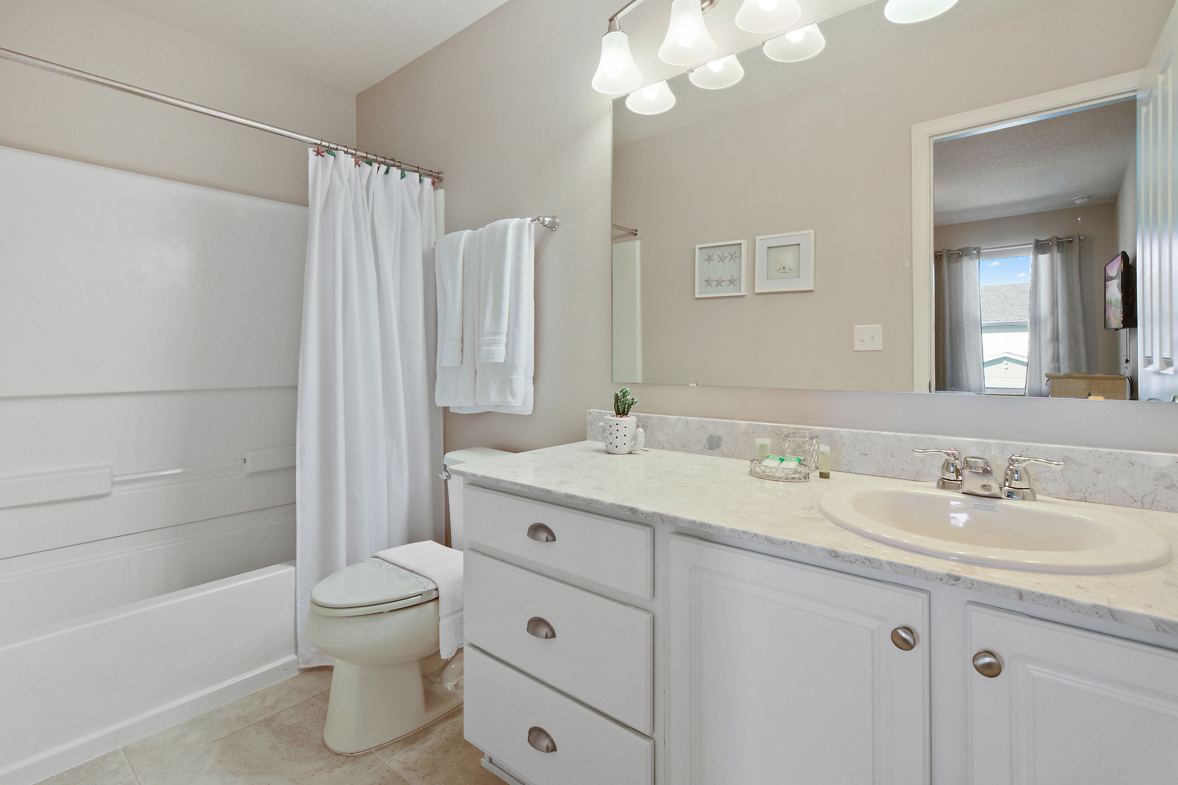 A bathroom with a bathtub, toilet, vanity with a sink, and a large mirror.