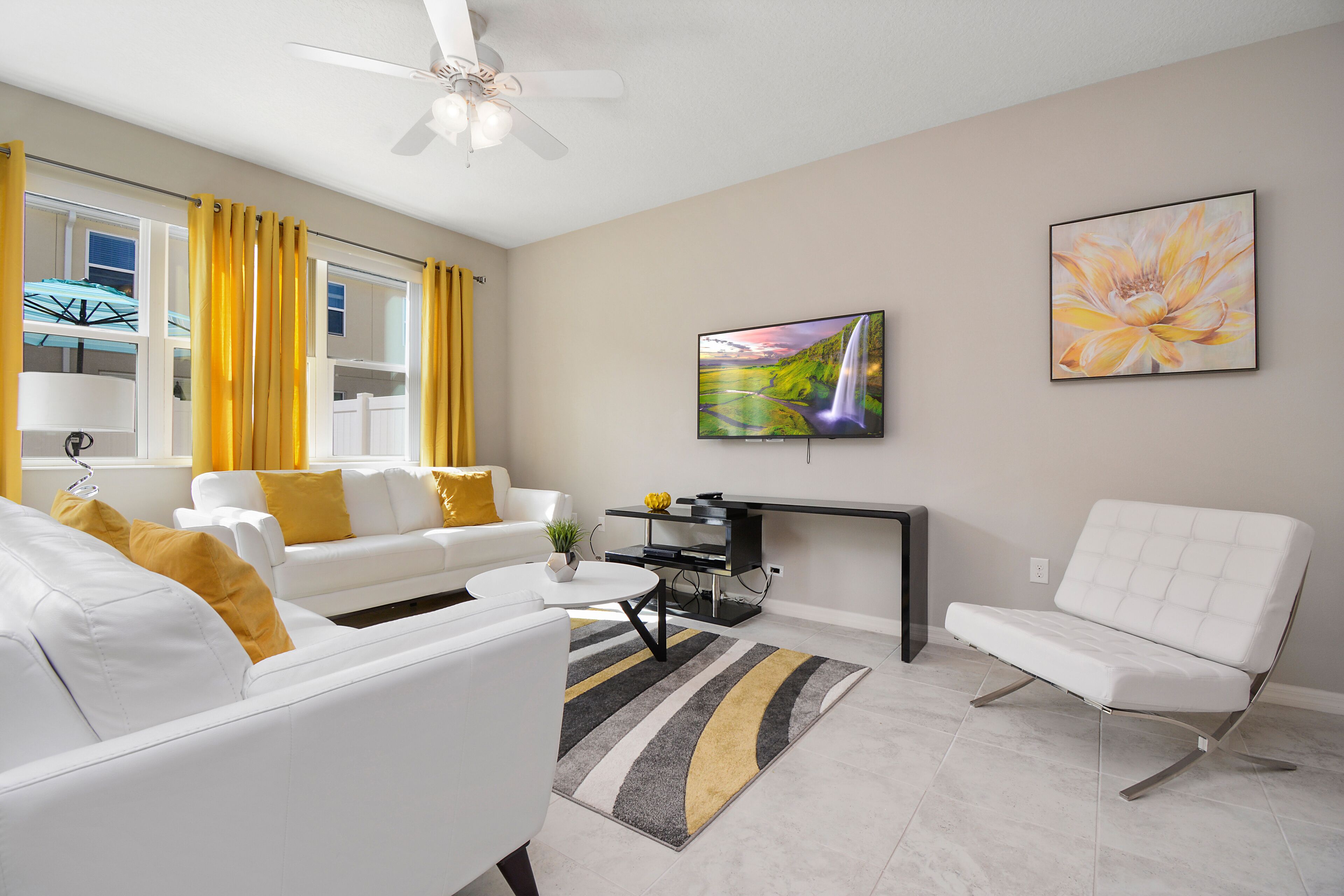 A modern living room with a white sofa, a white armchair, a coffee table, and a TV mounted on the wall.