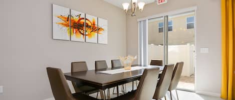 A conference room with a large table, chairs, and a chandelier. There is a glass door leading outside and an exit sign above it.
