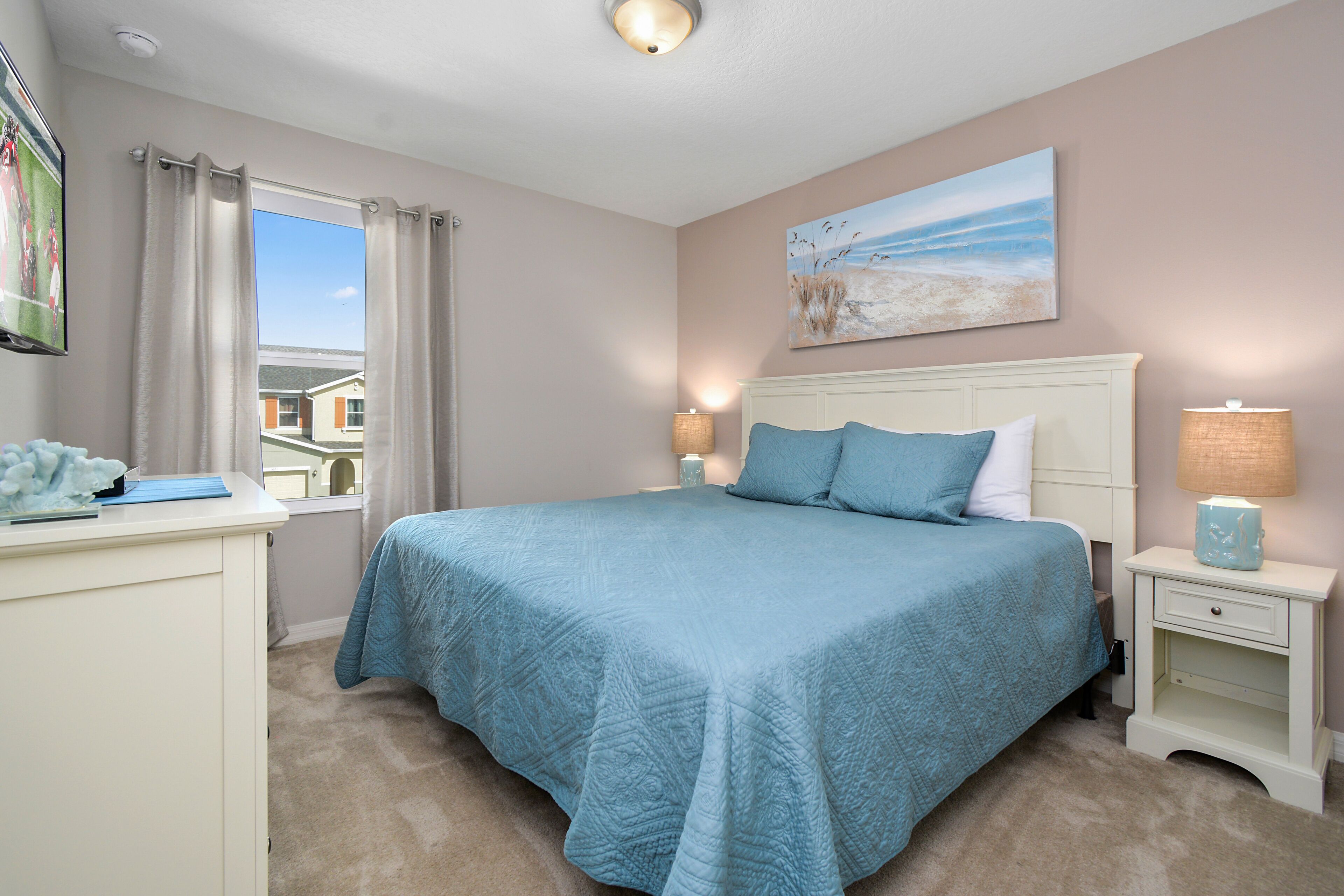 A bedroom with a large bed, a nightstand, a desk, and a window with curtains.