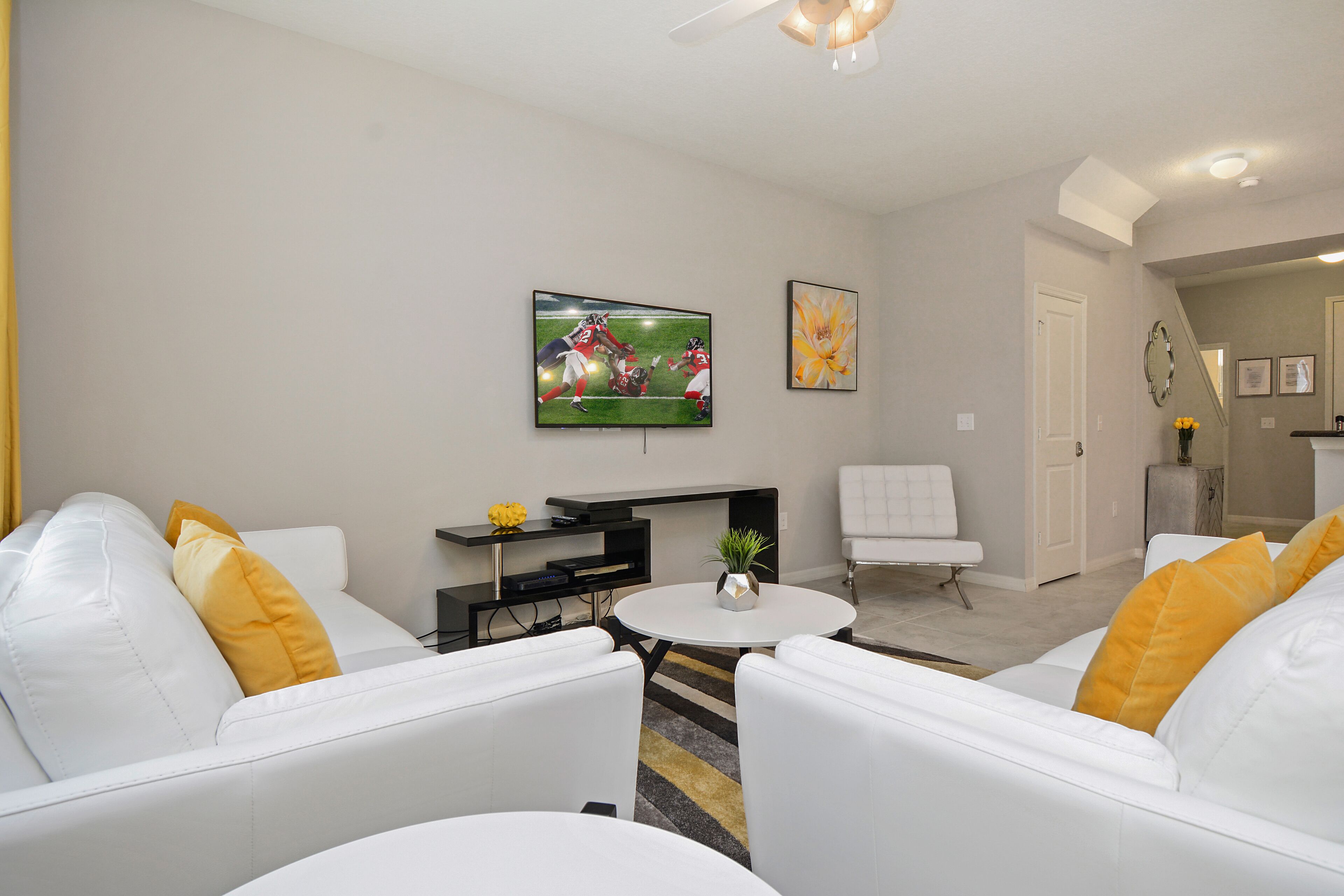 A modern living room with white sofas, a round coffee table, and a flat-screen TV mounted on the wall.