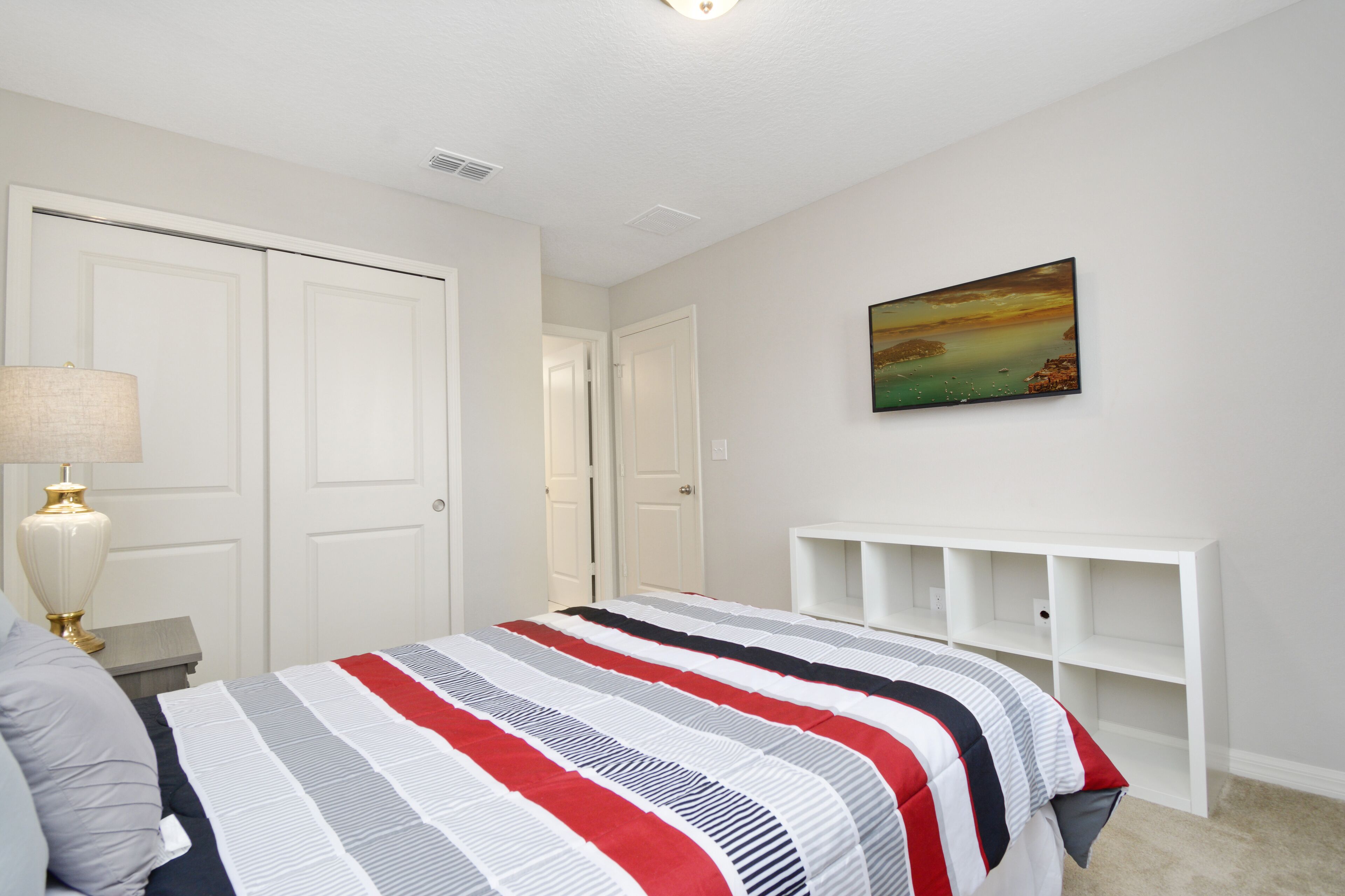 Een slaapkamer met een bed, nachtkastje, lamp, schilderij en een witte wandplank.