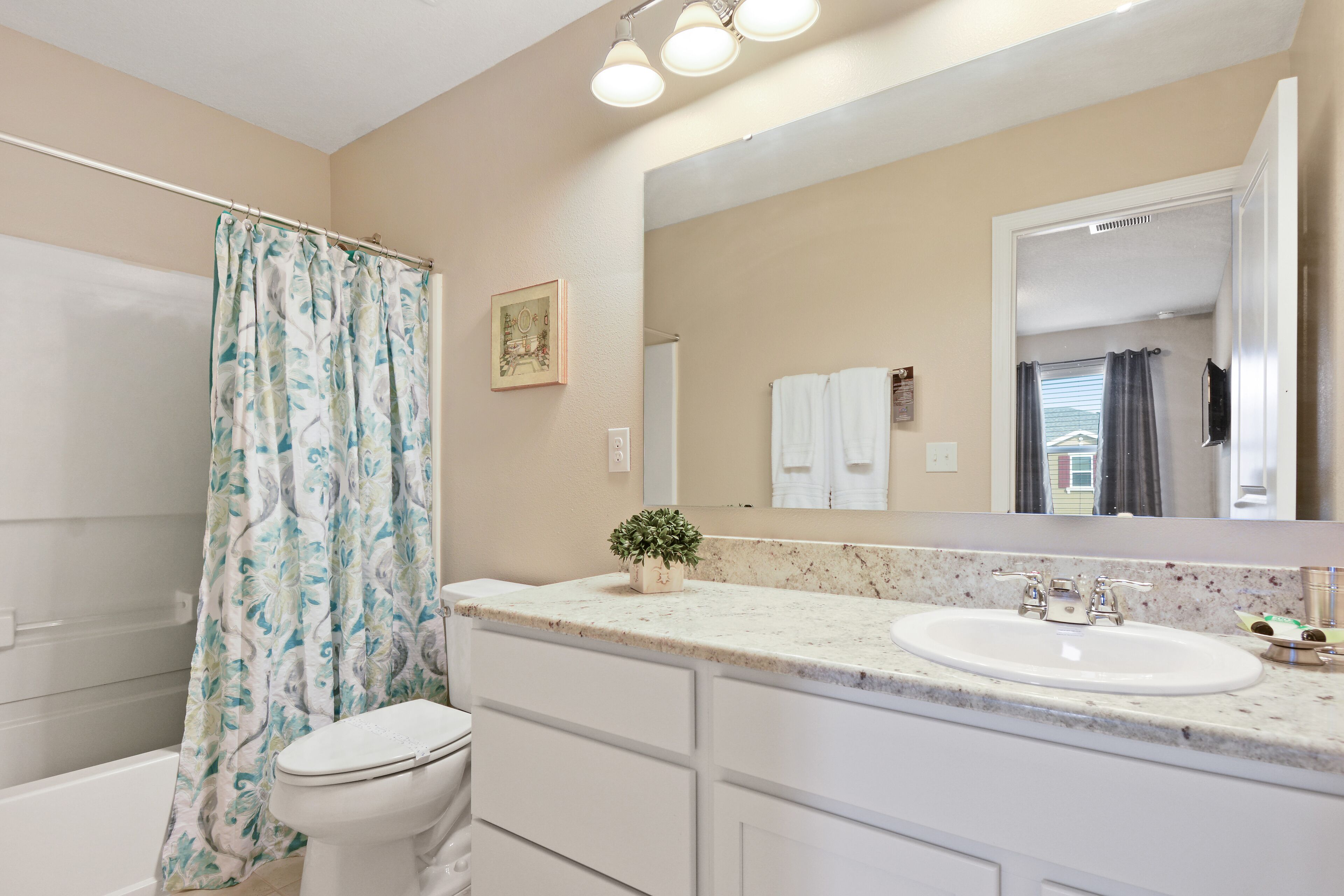 A bathroom with a shower curtain, toilet, sink, and a large mirror.