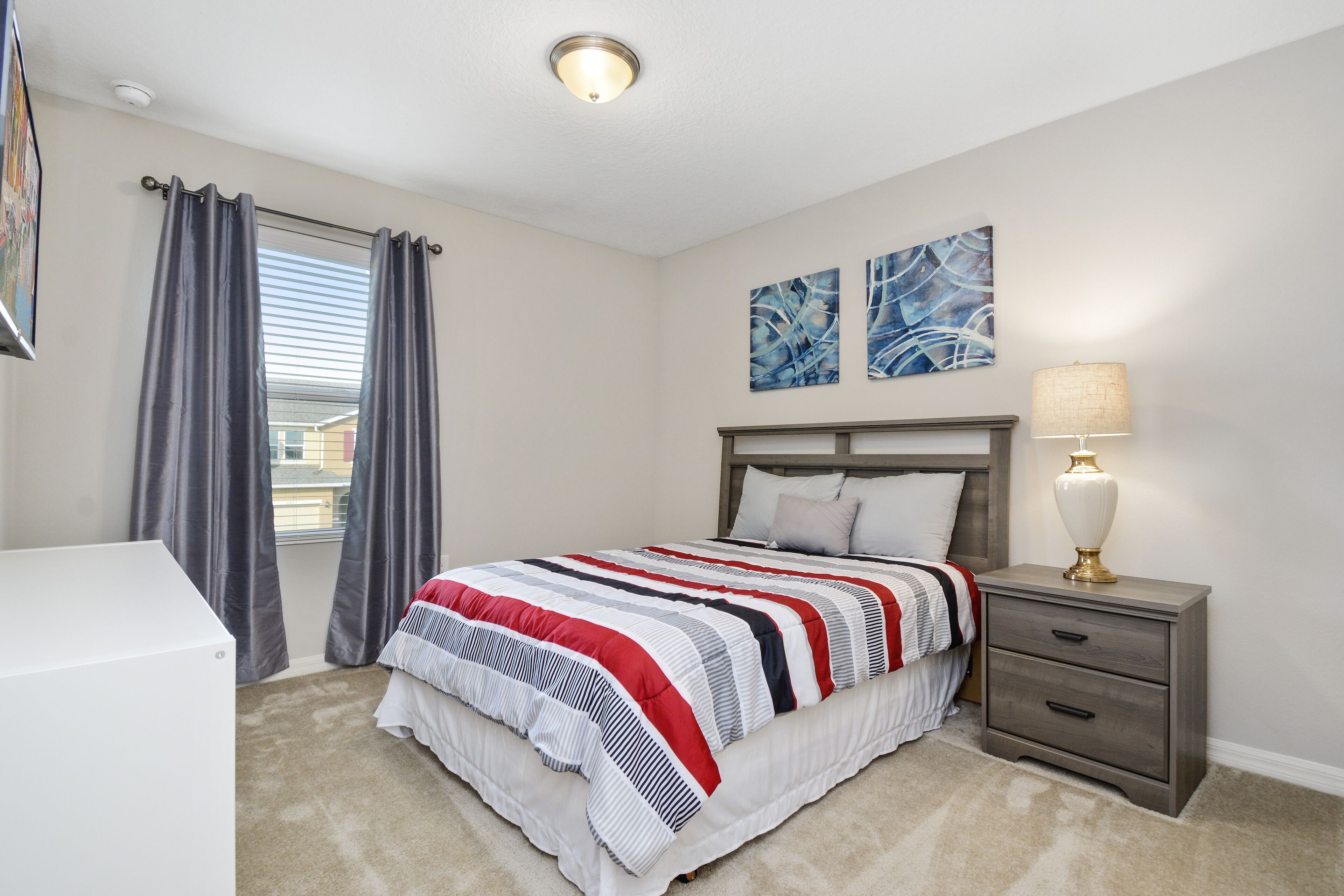 A bedroom with a bed, a nightstand, a lamp, and two abstract paintings on the wall.