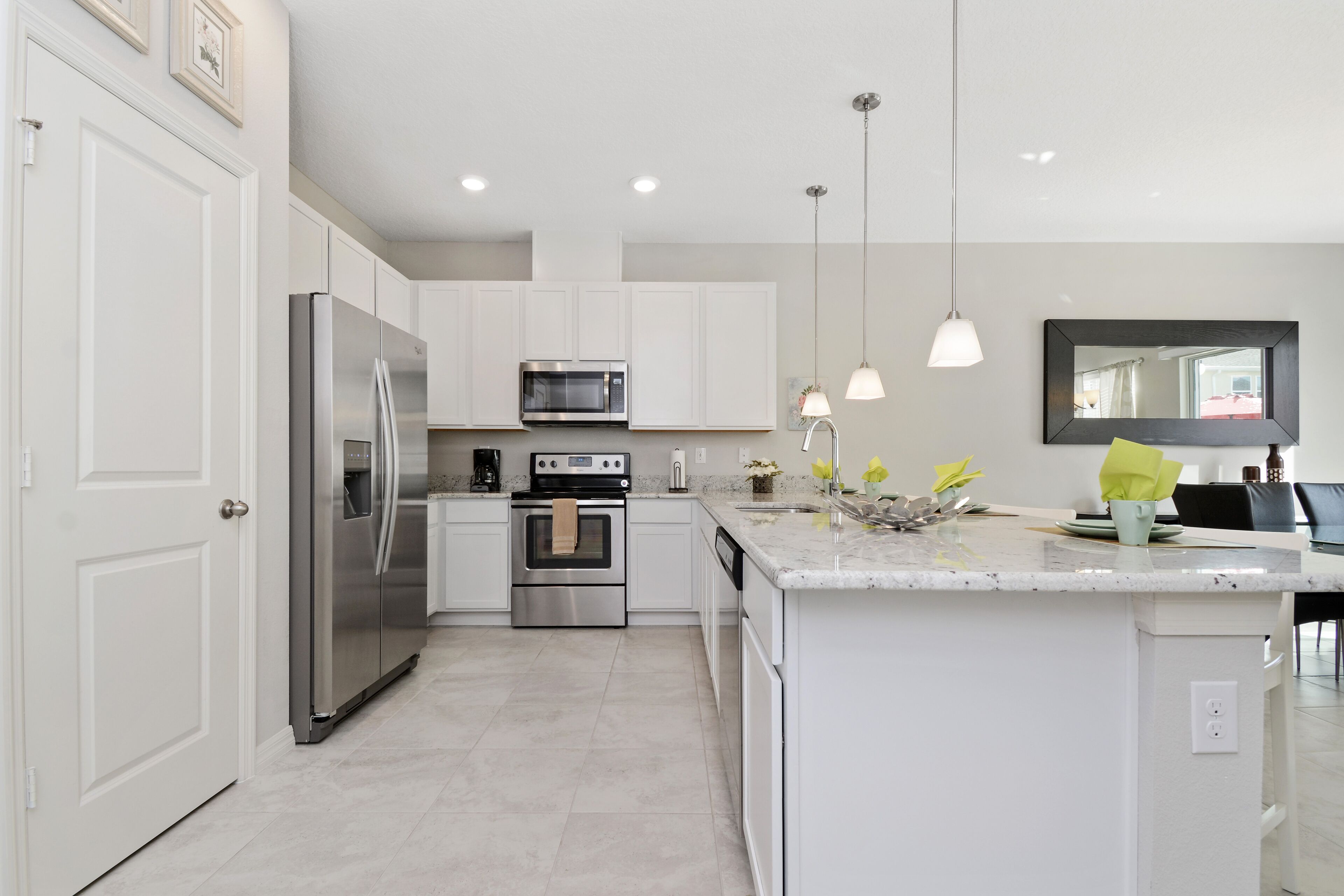 A modern kitchen with white cabinetry, stainless steel appliances, and pendant lighting.