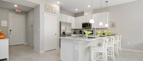 A modern kitchen with white cabinetry, a central island with bar stools, stainless steel appliances, and pendant lighting.