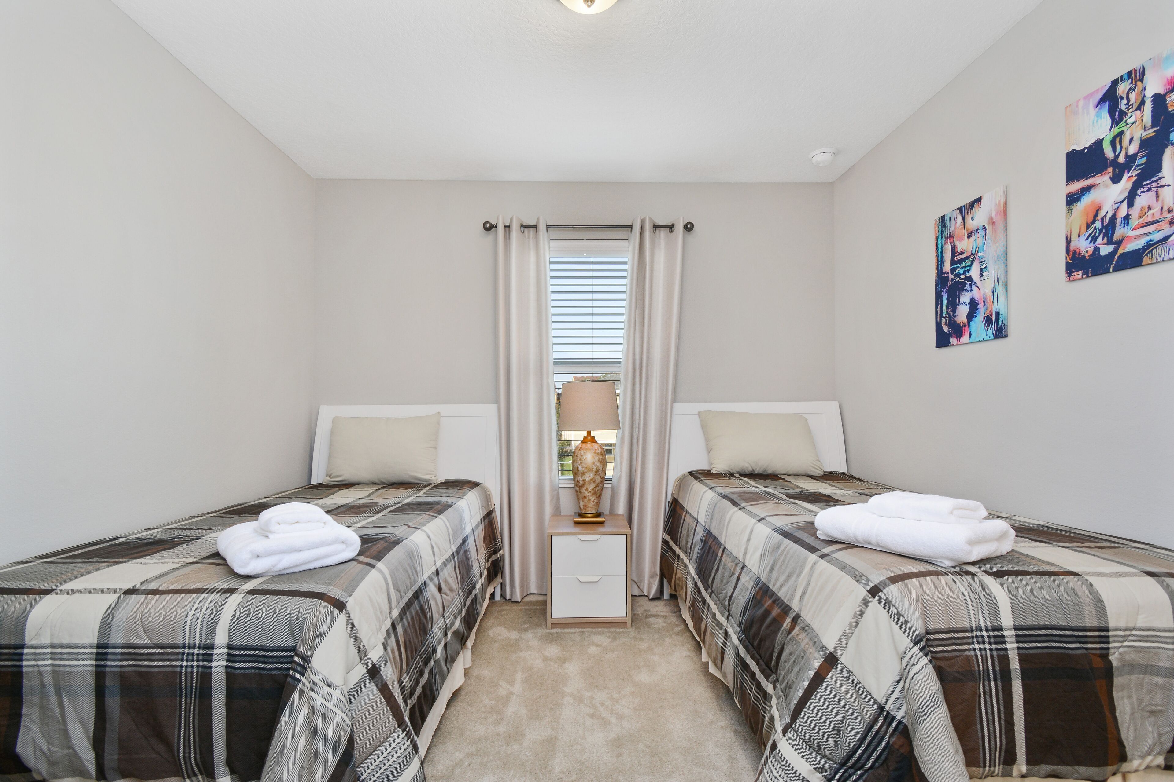 Une chambre avec deux lits, une table de chevet, une lampe et une fenêtre avec des rideaux.