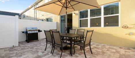 A patio with a table and chairs, a grill, and an umbrella.