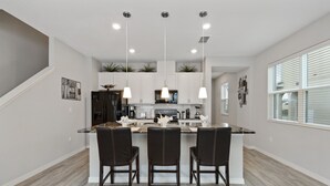 A modern kitchen with a central island, three bar stools, pendant lighting, and a staircase on the left. - Four Bedroom GameRoom Compass Bay Resort 5128A (Kissimmee)
