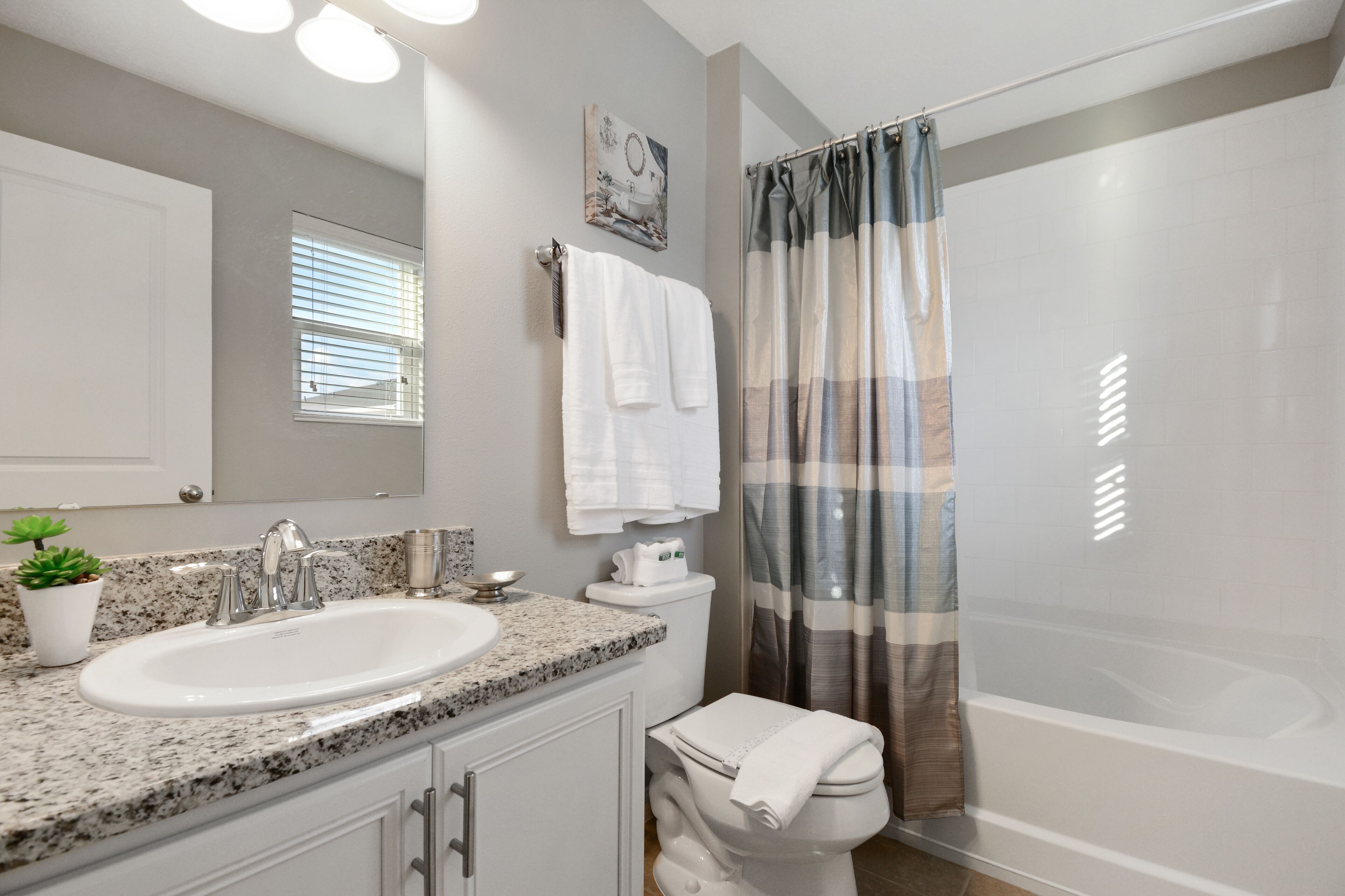 A modern bathroom with a granite countertop sink, a toilet, and a shower with a striped curtain.