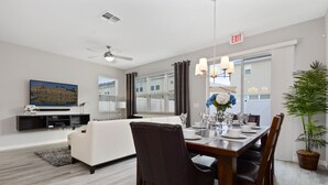 A modern living room with a dining area, a ceiling fan, a flat-screen TV mounted on the wall, a dining table set with chairs, and a potted plant. - Four Bedroom GameRoom Compass Bay Resort 5128A (Kissimmee)