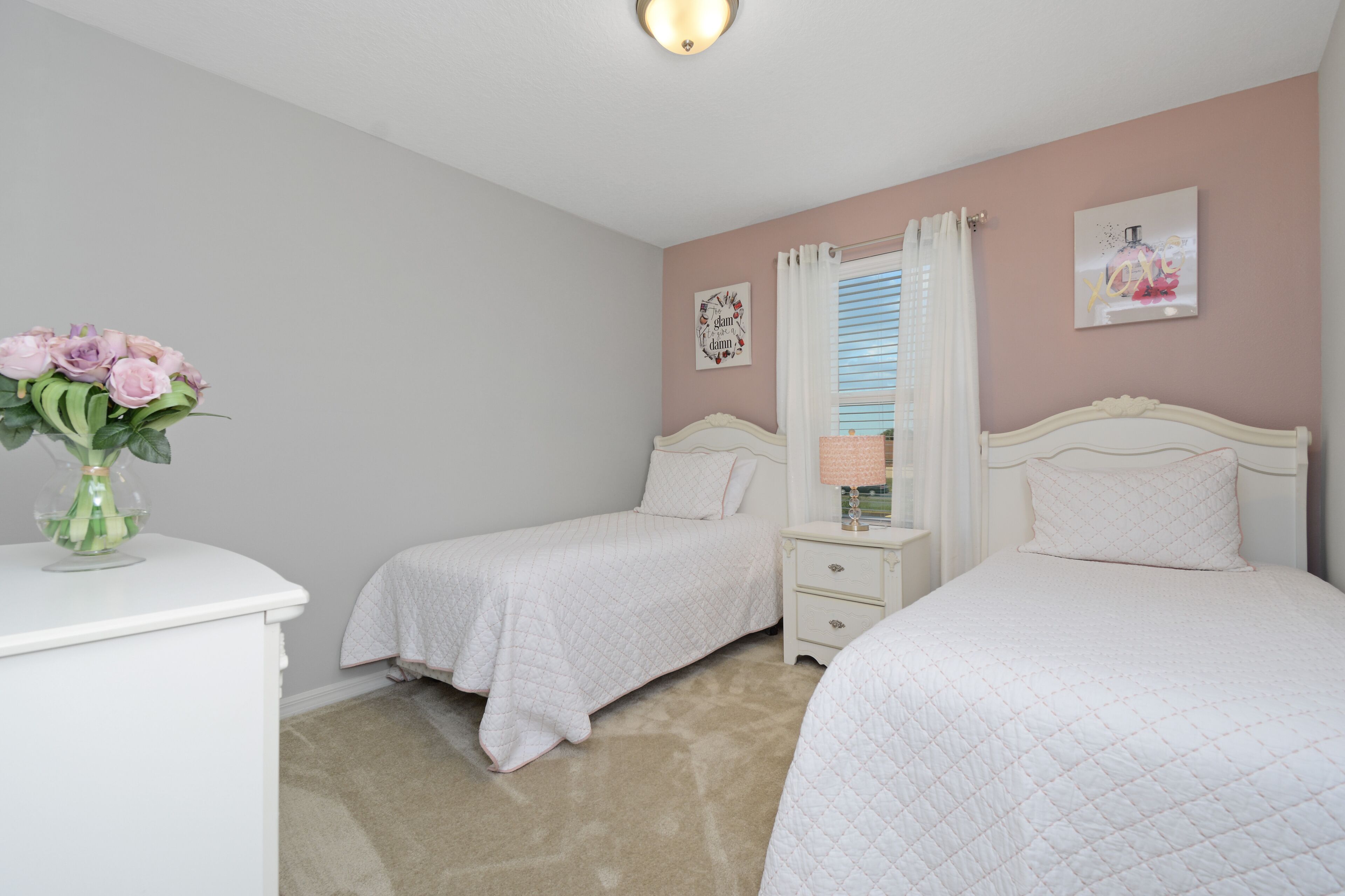 A bedroom with two beds, a nightstand, a dresser, and a vase with flowers.