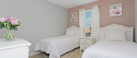A bedroom with two beds, a nightstand, a dresser, and a vase with flowers.