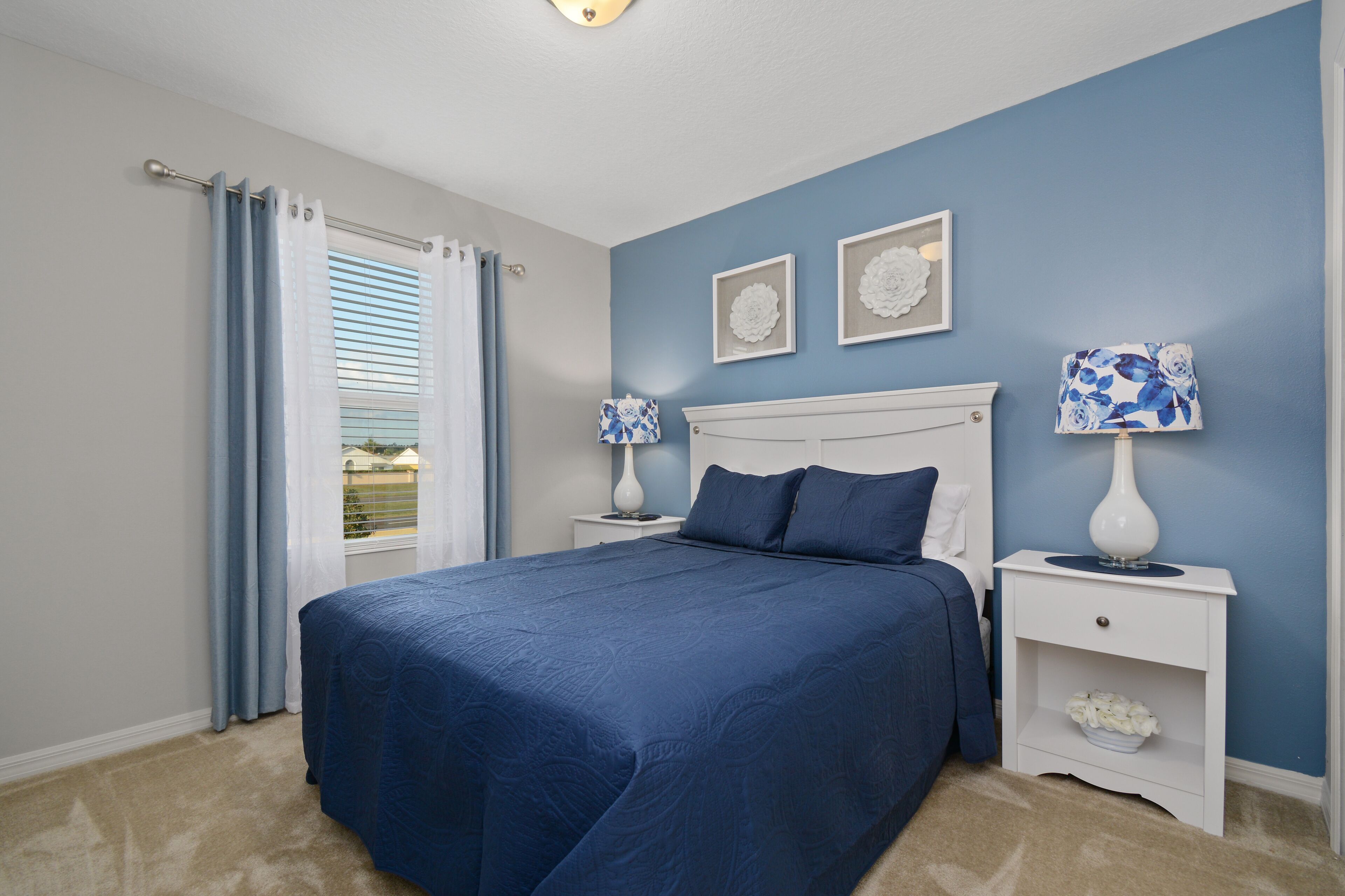 A bedroom with a large bed, two bedside tables, a nightstand, and a window with curtains.