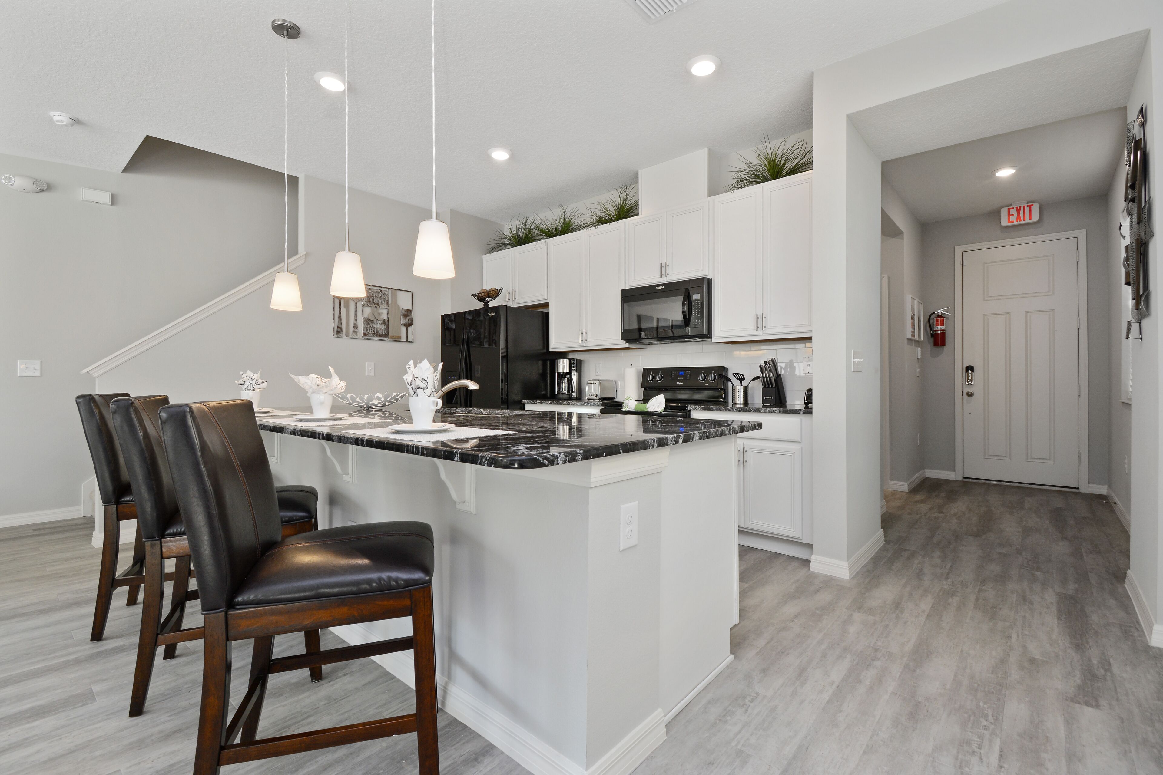 A modern kitchen with white cabinets, a black refrigerator, and a marble island with bar stools.