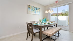A dining area with a table set for four, chairs, a bench, a hanging light fixture, and a painting on the wall. - Amazing 4 Bedroom Close to Disney @Compass Bay Resort 5161 (Kissimmee)