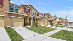 A row of townhouses with attached garages, a well-maintained lawn, and a clear sky. - Amazing 4 Bedroom Close to Disney @Compass Bay Resort 5161 (Kissimmee)