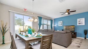 A modern living room with a dining area, a gray sofa, and a ceiling fan. - Amazing 4 Bedroom Close to Disney @Compass Bay Resort 5161 (Kissimmee)