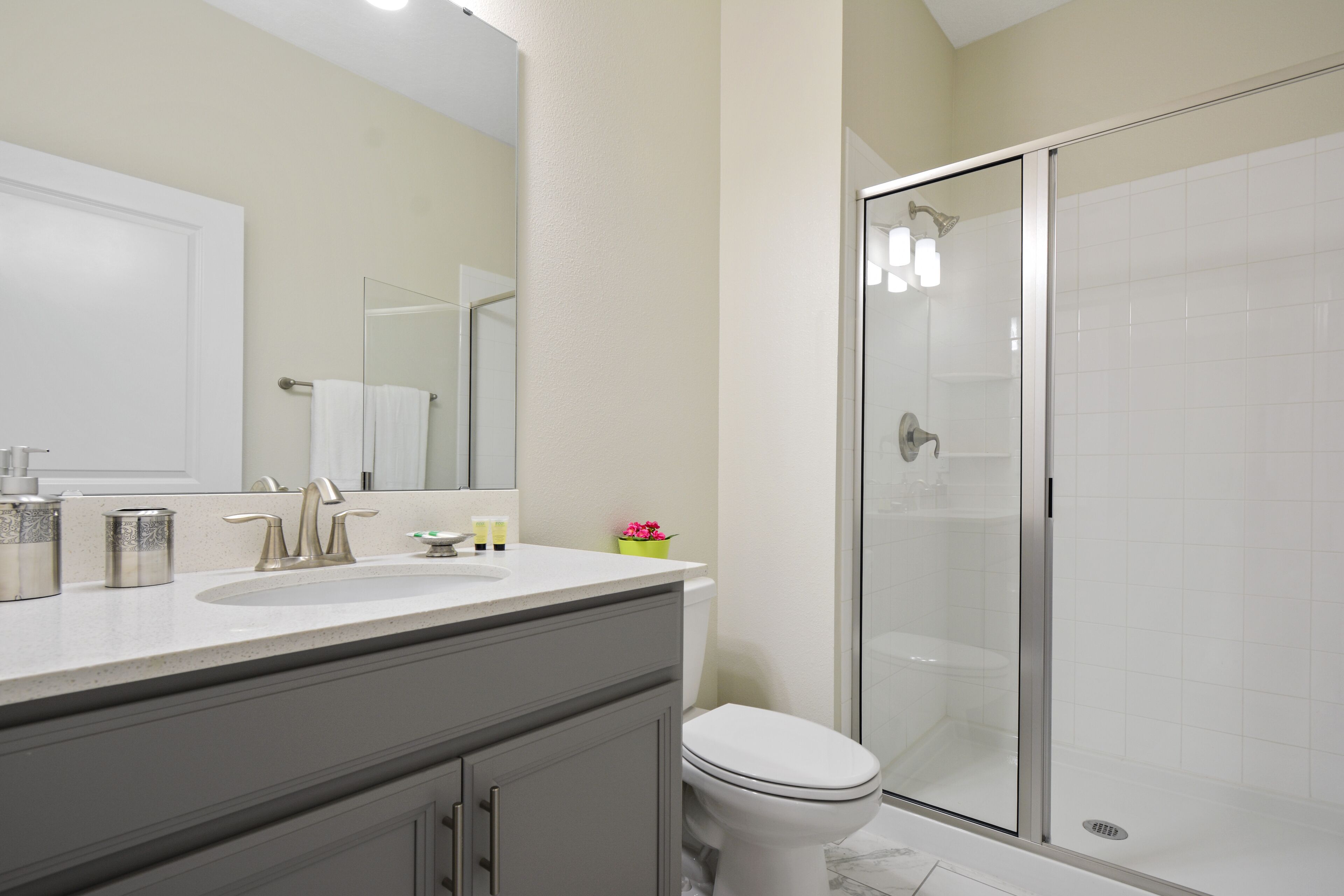 A bathroom with a white sink, mirror, and toilet, and a glass-enclosed shower area.