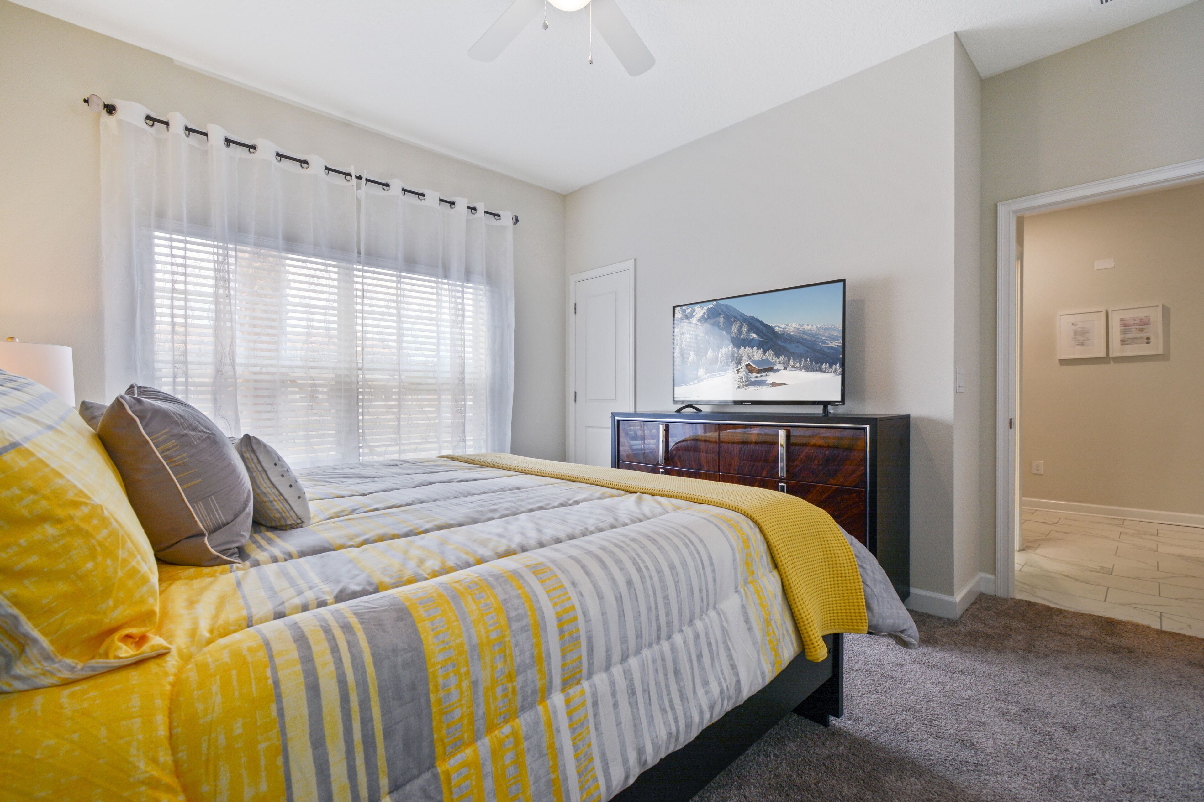 A bedroom with a bed, a television on a dresser, and a window with curtains.
