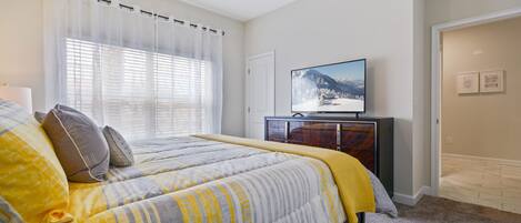 A bedroom with a bed, a television on a dresser, and a window with curtains.