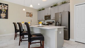 Una cocina moderna con una isla central, armarios grises, electrodomésticos de acero inoxidable e iluminación colgante.