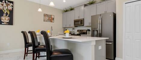 Una cocina moderna con una isla central, armarios grises, electrodomésticos de acero inoxidable e iluminación colgante.