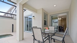 Un patio exterior con una mesa y sillas de vidrio, una piscina pequeña y vistas de la casa.