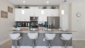 A modern kitchen with white cabinets, stainless steel appliances, and a central island with bar stools. - Four Bedroom Close to Disney w/ Screened Pool @StoreyLake 4910 (Kissimmee)