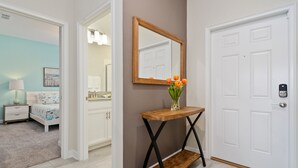 A hallway with a white door, a wooden console table with a mirror, and a vase with flowers. - Four Bedroom Close to Disney w/ Screened Pool @StoreyLake 4910 (Kissimmee)