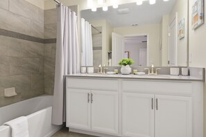 Un baño moderno con bañera, ducha con cortina, tocador con espejo y una planta en maceta.