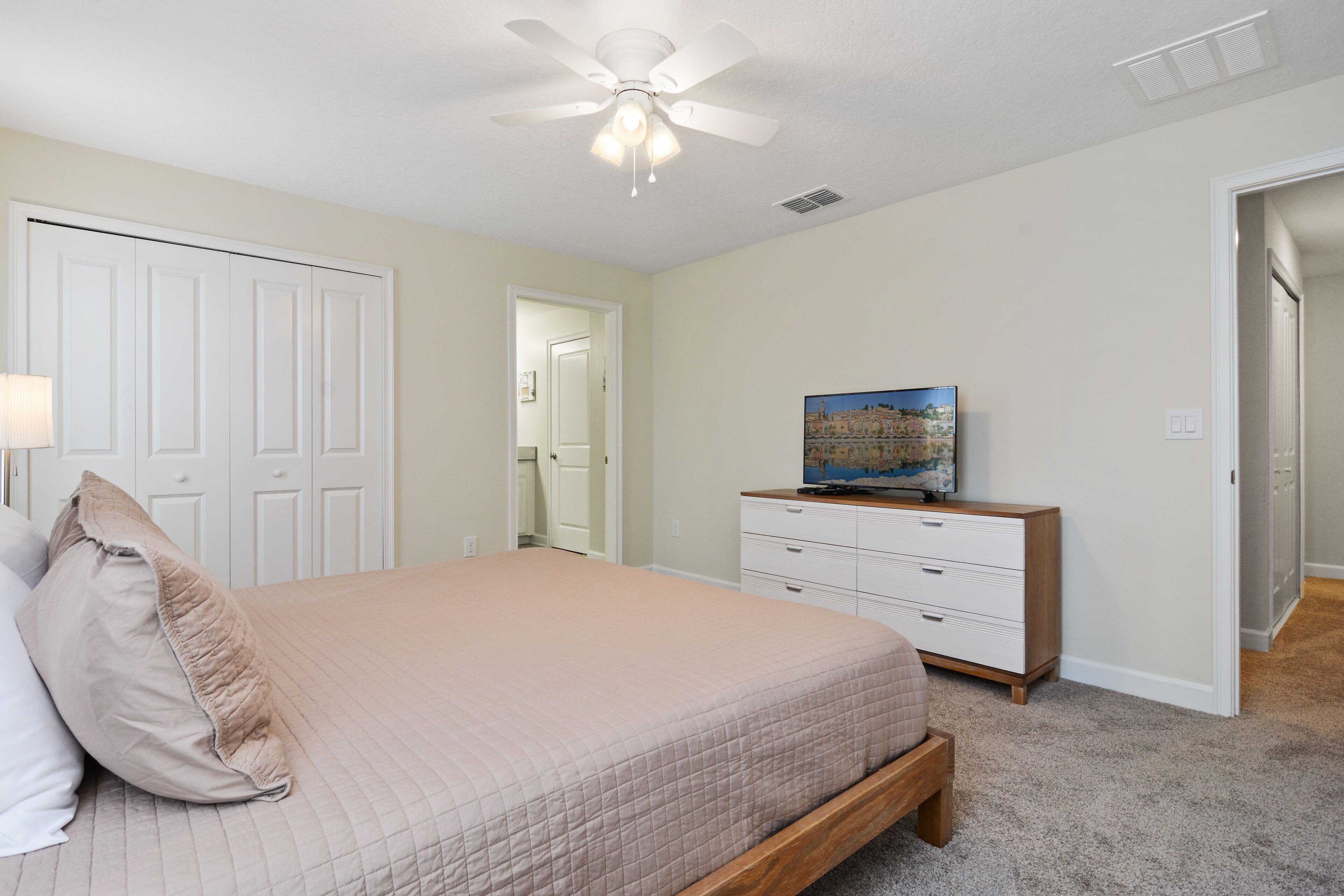 A bedroom with a bed, a dresser, a ceiling fan, and a painting on the wall.