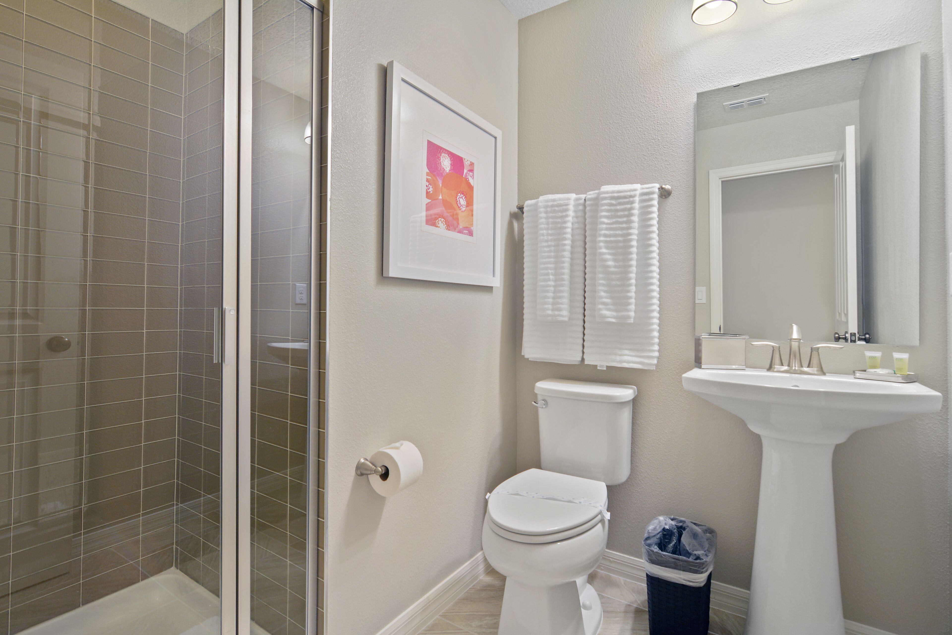 Une salle de bain avec une douche à parois de verre, des toilettes, un lavabo et un tableau encadré au mur.