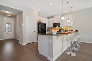A modern kitchen with white cabinetry, a black refrigerator, and a bar area with stools. - Stunning 4Bd Sleeps9 w Jacuzzi Close to Disney @ Compass Bay 5113 (Kissimmee)