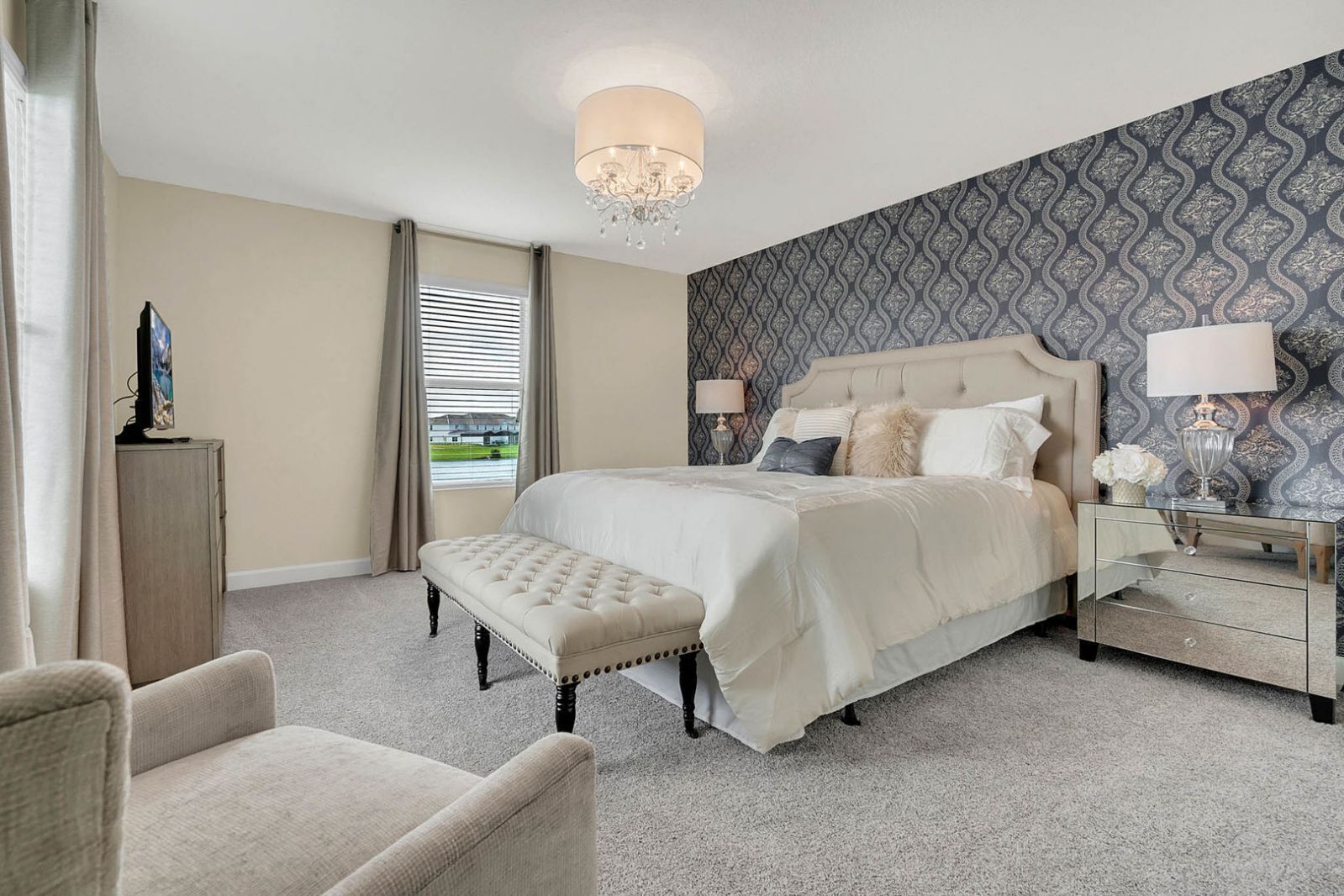 A hotel bedroom with a large bed, a bench, a nightstand, and a chandelier.