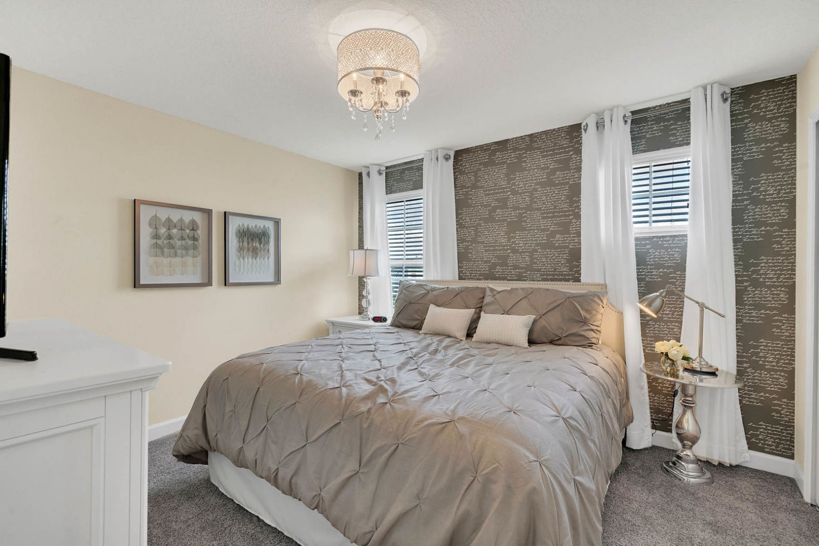 A bedroom with a large bed, a chandelier, a nightstand, and a wall with decorative script.