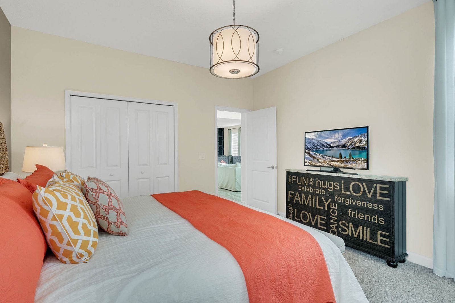 A bedroom with a bed, pillows, a bedside lamp, a dresser with a word cloud decoration, and a painting on the wall.