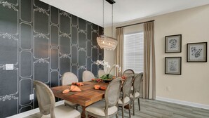 Ein Essbereich mit Holztisch, sechs Stühlen, einer Chandelierleuchtreibe und Wandpapier mit Schwarz-Weiß-Muster.