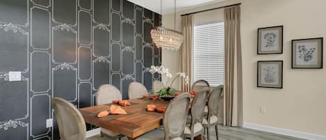 A dining area with a wooden table, six chairs, a chandelier, and black and white patterned wallpaper.