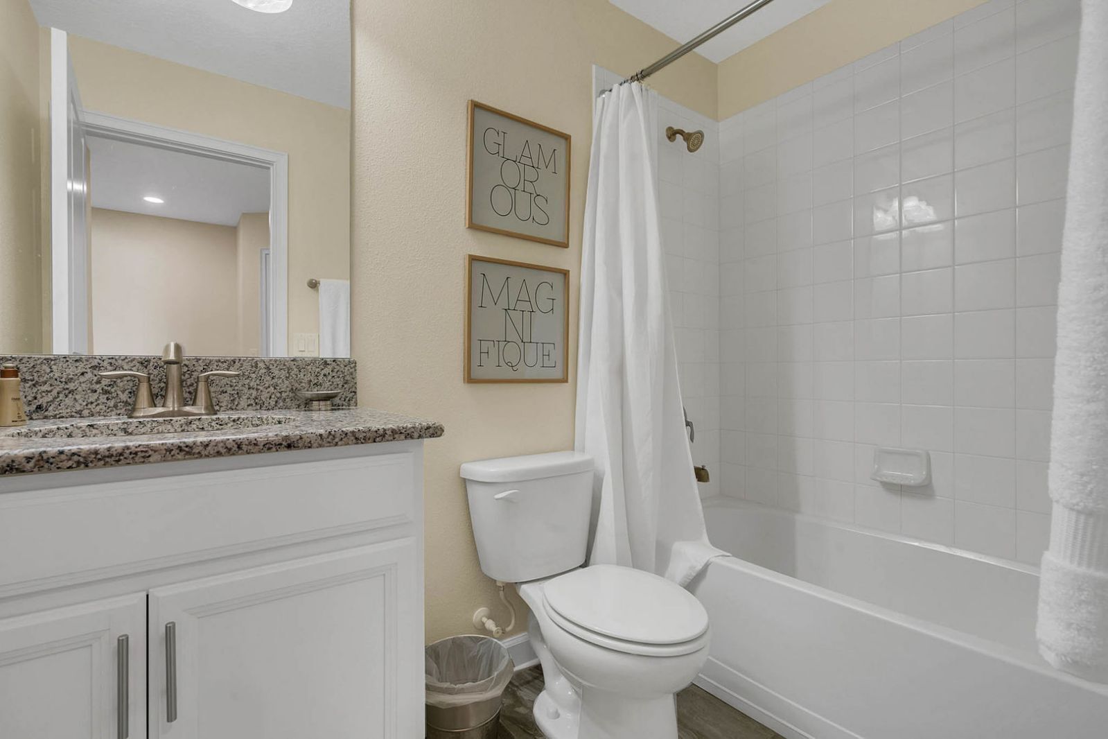 A bathroom with a white toilet, a shower with a curtain, a granite countertop, and two framed motivational quotes on the wall.