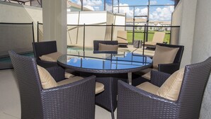 A glass-enclosed patio with wicker furniture and a pool.