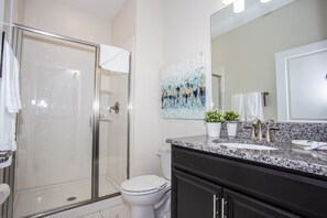 Une salle de bain moderne avec une douche à parois de verre, des toilettes blanches, un comptoir en granit et un grand miroir.