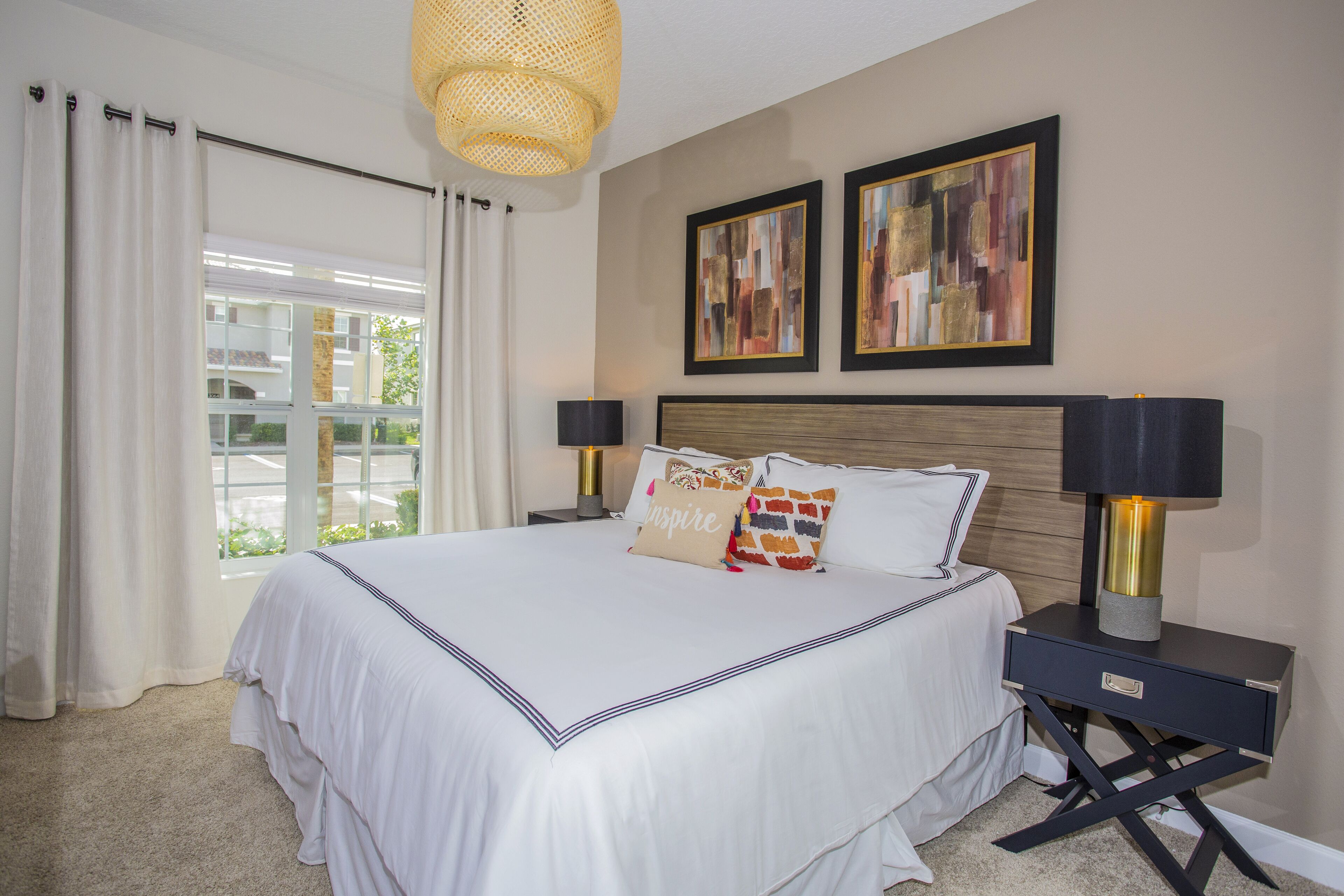 A neatly made bed with white bedding and decorative pillows, a bedside table with lamps, and two framed artworks on the wall.